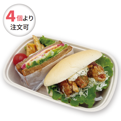 To-go tray with a fried chicken sandwich and a club sandwich, greens, shredded cabbage, a cherry tomato, and potato wedges; round badge reads 'Order from 4 pieces' (Japanese).