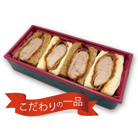 Sliced roast meat arranged in a red rectangular takeout tray with a red ribbon label reading 'こだわりの一品'